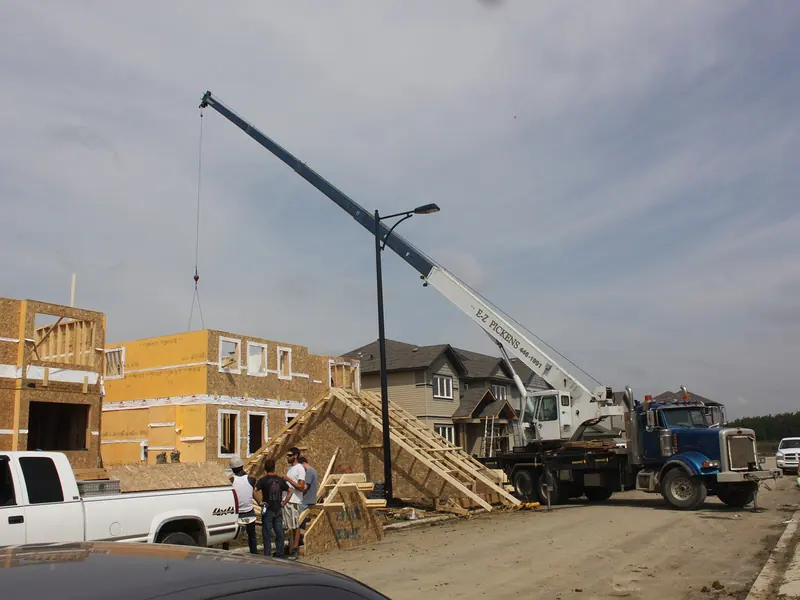 Truck crane lifting materials onto a wood-frame building under construction